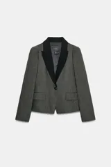 Blazer Zara Woman Collection de corte estructurado en tejido de espiga gris, con solapas de muesca en contraste color negro. Presenta cierre frontal con un botón, mangas largas y bolsillos delanteros con solapa.