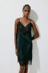 Vestido corto lencero de satén negro, con escote en V pronunciado y ribetes de encaje floral en el escote y el bajo. Cuenta con finos tirantes spaghetti cruzados en la espalda.