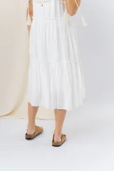 Vestido largo blanco de algodón con escote en V, breteles finos regulables con lazo y borlas, y detalle de tejido artesanal en el escote.