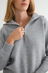 Buzo de punto gris con cuello polo y cierre frontal parcial, de manga larga y diseño holgado con puños y ruedo acanalados.