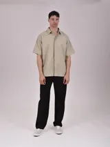Camisa de manga corta en color blanco, con cuello clásico y cierre frontal oculto mediante botones. Presenta un diseño minimalista de corte recto.