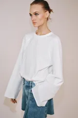 Falda corta de tiro medio confeccionada en tejido denim de algodón. Presenta diseño con tablas, bolsillos delanteros, cintura con trabillas y bajo desflecado. Cierre frontal con cremallera, botón y ganchos metálicos.