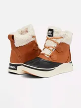 Bota de invierno impermeable Sorel modelo Out N About IV Chill, confeccionada en cuero marrón con puntera y base de goma negra, suela gruesa de goma blanca, y detalles de forro y cuello de borrego sintético blanco con cordones tostados.