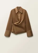 Camisa de ramio color tostado con cuello camisero, manga larga con puños abotonados y cierre frontal parcial con tres botones. Presenta un diseño cruzado en el frente y bajo asimétrico.