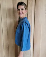 Blusa blanca de manga larga con cuello alto y volados en cuello y hombros.