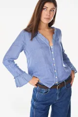 Blusa de lino italiano color azul, con escote en V y botones de nácar en la parte frontal. Presenta detalles de volados en el cuello y en los puños de las mangas largas.