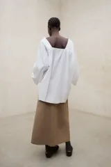Blusa blanca de corte amplio y diseño off-shoulder, con escote en V cruzado y mangas largas holgadas.