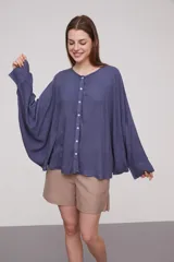 Camisa de corte holgado y diseño amplio, con cuello redondo y cierre frontal de botones. Presenta mangas largas con caída fluida y puños sencillos.