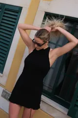 Vestido corto negro de punto smock, sin mangas, con cuello alto y detalle de volado en el ruedo.
