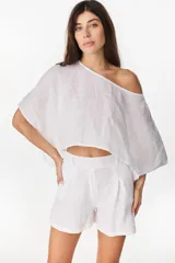 Blusa de lino italiano color blanco, con diseño holgado, escote asimétrico estilo off-shoulder y mangas cortas amplias.