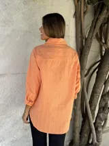 Camisa color salmón con cuello clásico, cierre frontal con botones y mangas largas con puños abotonados.