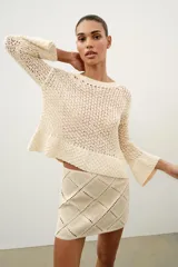 Minifalda de tiro medio confeccionada en ante color beige, decorada con aplicaciones de tejido tipo crochet blanco formando un patrón de rombos. Cuenta con cierre de cremallera oculta en la costura.