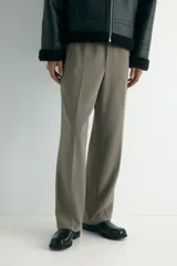Pantalón de corte relajado y pierna recta, confeccionado en tejido suave de color marrón. Presenta cintura elástica con cordón de ajuste, pliegues frontales y traseros, bolsillos laterales y un bolsillo posterior insertado.