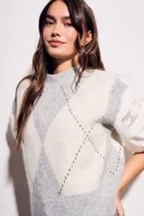 Chaleco de tejido de punto con diseño de rombos en tonos gris claro y blanco. Presenta mangas abullonadas de tela blanca con detalles de encaje y cuello redondo.