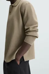 Polo de punto de manga larga con cuello solapa y cierre frontal de botones. Presenta un diseño de corte regular con aberturas laterales en el bajo.