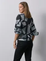 Blusa de gasa con estampado geométrico en tonos negro, gris y celeste. Tiene cuello redondo y mangas 3/4 amplias con abertura y botón.