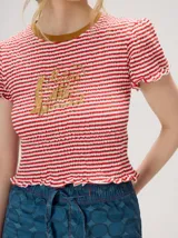 Remera baby-tee a rayas verde y blanca con cuello redondo rojo y gráfico impreso en la parte delantera, de manga corta y textura fruncida.