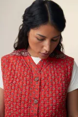 Chaleco sin mangas de algodón acolchado con estampado floral en tonos rojos y marrones. Tiene cuello camisero, cierre frontal con botones de madera y bolsillos de parche. El modelo Patchwork Tomette está tejido a mano.