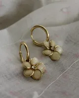 Aros tipo argolla pequeña con dije colgante en forma de flor de cinco pétalos color crema con centro de cristal, elaborados en acero quirúrgico dorado.