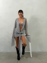 Vestido corto de tejido liviano y semitransparente en color gris, con mangas largas acampanadas y diseño frontal con nudo ajustable en la cintura.