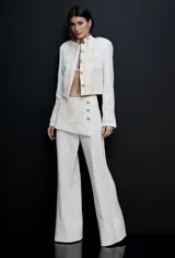 Chaqueta de mujer con estructura de sastrería e inspiración militar, de color blanco. Presenta bordados ornamentales claros en el frente y las mangas, botones metálicos dorados y hombros definidos con corte corto.