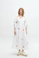 Vestido midi blanco de algodón con bordados de motivos marinos, escote en V, mangas 3/4 abullonadas y abotonadura frontal.