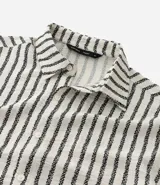 Camisa de manga larga con cuello inglés y cierre frontal de botones. Presenta un diseño de rayas verticales en tonos neutros, confeccionada en tejido de poliéster con caída estructurada y corte comfort.