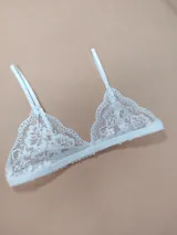 Bralette de encaje blanco con diseño triangular, tirantes finos regulables y banda elástica inferior.