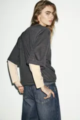 Jersey de cuello redondo y manga larga con diseño de doble capa, combinando un cuerpo en tono gris oscuro con mangas en tono beige.