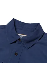 Camisa de manga larga Caterpillar de color azul, confeccionada en mezcla de tencel y algodón. Cuenta con cuello clásico, cierre frontal de botones, dos bolsillos en el pecho con solapa y botones, y diseño con mangas convertibles tipo roll-tab.