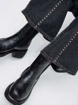 Bota corta tipo chelsea de cuero vacuno negro con textura grabada de motivos florales. Presenta paneles elásticos laterales, puntera redondeada y suela con plataforma y taco cuadrado.