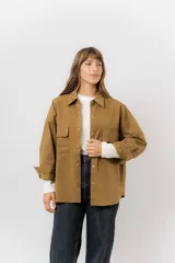Sobrecamisa de gabardina liviana color crema, con corte oversize, cuello clásico, cierre frontal con botones a presión y dos bolsillos delanteros con solapa.
