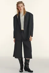 Blazer oversize de corte recto con cuello de solapa, manga larga con hombreras y cierre frontal de doble botonadura. Presenta un diseño en color gris oscuro con costuras decorativas a contraste en color blanco, bolsillos con solapa y forro interior.