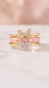 Set de tres anillos apilables de plata 925 con baño de oro. Incluye un anillo con dije de corazón pavé de circonias, un anillo con esmalte rosa y detalles de corazones, y un anillo con diseño de lazo de Minnie Mouse decorado con circonias.