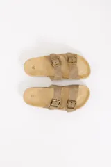 Sandalias planas estilo Birkenstock en color beige, con dos tiras ajustables mediante hebillas metálicas en tono bronce. Cuenta con plantilla anatómica y suela de corcho y goma.