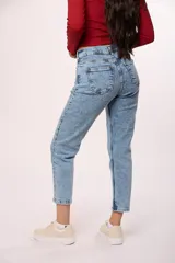 Jean de corte mom con tiro alto, confeccionado en denim de lavado claro con efecto desgastado. Presenta un diseño clásico de cinco bolsillos, cierre con cremallera y botón metálico.