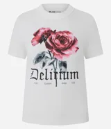 Remera de algodón con cuello redondo y mangas cortas. Presenta un estampado frontal con rosas en tonos rojizos y la palabra 'Delirium' en tipografía gótica, junto con detalles de texto adicionales.