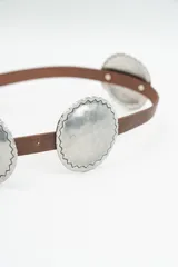 Cinturón de cuero negro con apliques circulares metálicos plateados con bordes dentados.