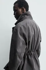 Cazadora relaxed fit de hombre, confeccionada en tejido técnico con algodón de color negro. Cuenta con cuello camisero, manga larga y bolsillos frontales de plastrón con solapa. Presenta cintura ajustable con cordón interior y cierre frontal con cremallera oculta por solapa con botones a presión.