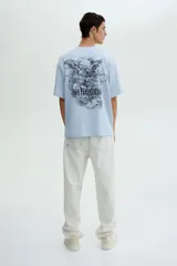 Remera de algodón color celeste con cuello redondo acanalado, mangas cortas y hombros caídos. Presenta un estampado gráfico central con alas y la frase 'No Regret'.