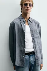 Camisa de corte relajado confeccionada en tejido fluido con mezcla de viscosa, presenta un diseño de rayas verticales, cuello solapa, cierre frontal con botones, manga larga con puño abotonado y un bolsillo de plastrón en el pecho.