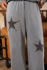 Pantalón gris de corte amplio y fluido, con bolsillos laterales y apliques de estrellas negras con contorno dorado en ambas piernas.