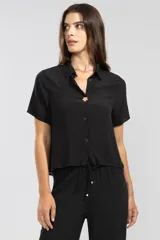 Camisa negra de manga corta en crepé de viscosa suave, con cuello camisero, detalle de flor Polonio en cobre y bolsillos laterales.