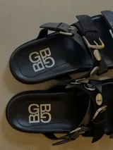 Sandalias de cuero marrón, con diseño de triple tira con hebillas, detalles de tachas y apliques de pelo con estampado animal print.