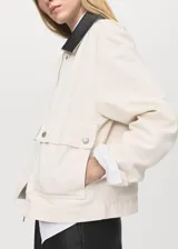 Chaqueta recta de algodón estilo vaquero, color blanco, con manga larga, cuello camisero de efecto piel en contraste, cierre oculto de cremallera y botones, y dos bolsillos delanteros de parche con solapa.