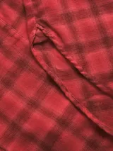 Camisa de franela twill color rojo con patrón de cuadros en tonos oscuros, corte relajado, mangas largas, cuello camisero, cierre frontal con botones y un bolsillo aplicado en el pecho.