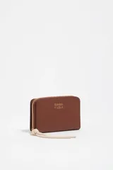 Billetera Bimba y Lola color marrón, de estructura rígida en piel vacuna, con cierre de cremallera y tirador de cordón en color crudo. Incluye logo de la marca estampado en dorado en el frente.