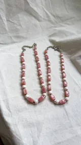 Collar de cuentas rectangulares de color rosa y cuentas esféricas de vidrio blanco, intercaladas con pequeñas piezas de hematita plateada. Cuenta con una cadena de extensión metálica.