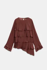 Blusa marrón de cuello redondo y manga larga, con volantes horizontales superpuestos y bajo asimétrico. Cuenta con detalle de abertura y botón en la espalda.