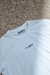 Remera blanca de manga corta con cuello redondo, pequeña estampa frontal y etiqueta decorativa en el borde inferior.